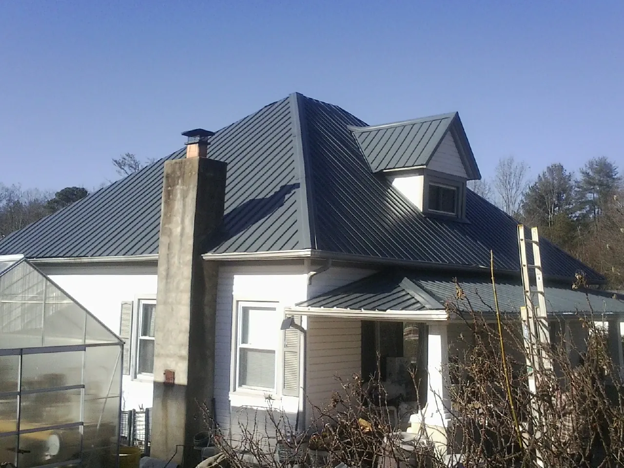 Dark blue standing seam metal roof on a white farmhouse with dormer — Slate & Tile Roof Repair by Roofing Brothers in Preston Park
