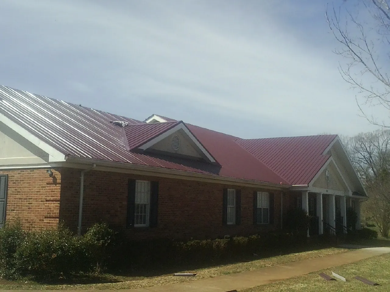 Red metal roof with gabled entries on a long brick building, from a Hail Damage Roof Repair job in Preston Park