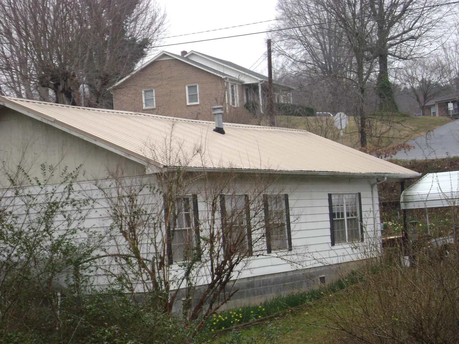 Tan metal roof on a white sided house set into a hillside — Commercial Roofing by Roofing Brothers in Preston Park