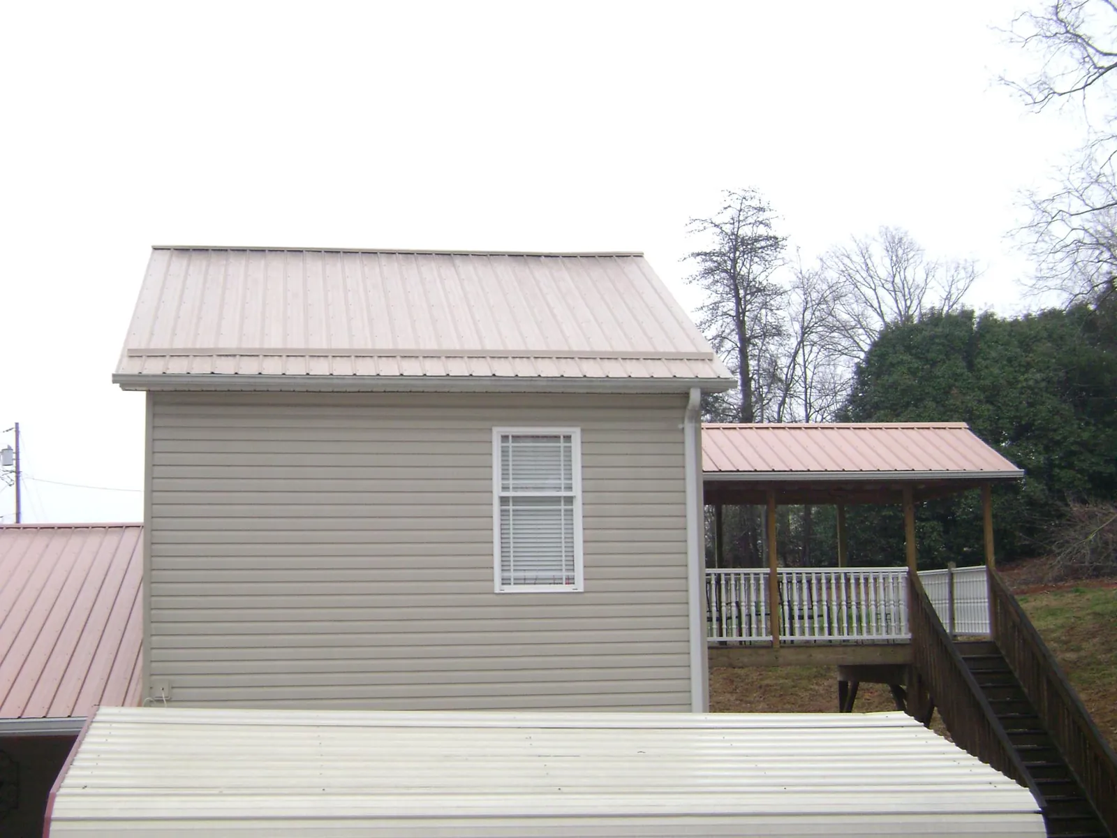 Tan metal roofs on a two story addition and attached porch, from a Roof Replacement job in Preston Park